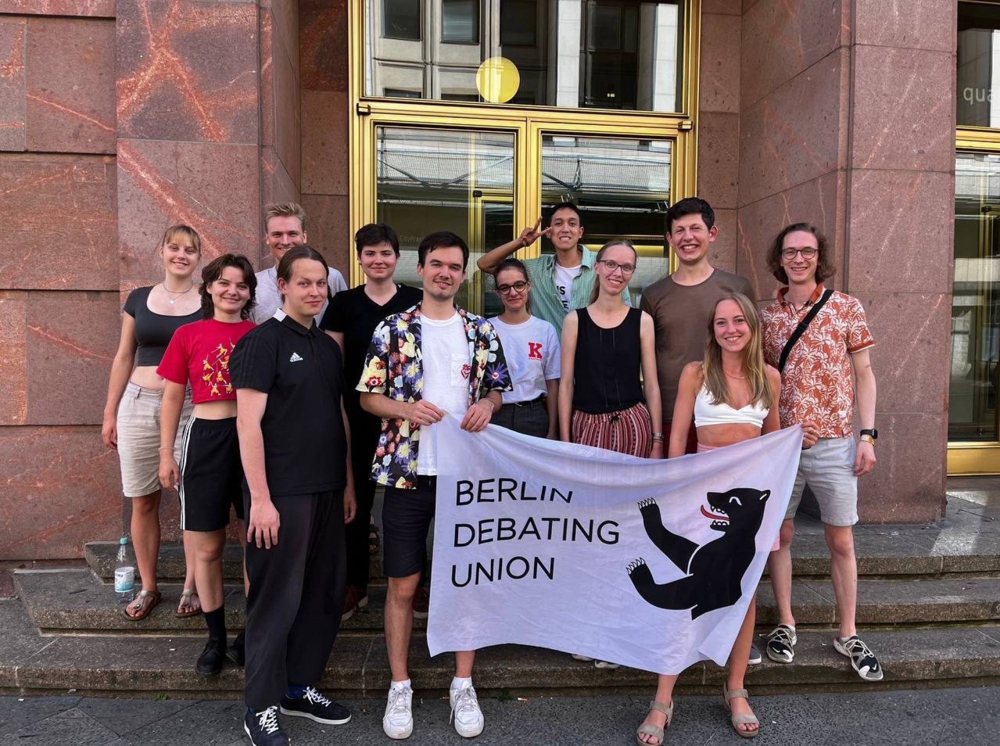 Mitglieder der Berlin Debating Union mit ihrer Clubflagge vor der Humboldt-Universität